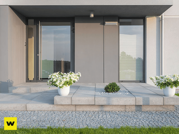 Moderner Hauseingang mit grauen Fliesen, Glasfront und weißen Blumentöpfen im Vorgarten.