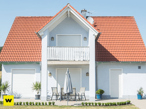 Modernes Einfamilienhaus mit rotem Dach, Balkon und Terrasse an sonnigem Tag.