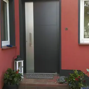 Moderne anthrazitfarbene Haustür mit Seitenteil an roter Fassade, Eingangstreppe