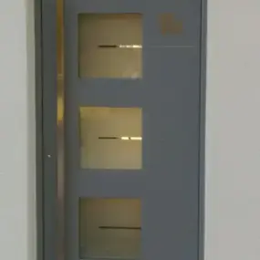 Graue moderne Haustür mit drei Glasfenstern und langem Edelstahlgriff