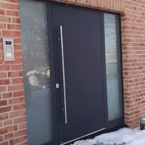 Moderne schwarze Haustür mit Seitenteilen aus Glas an roter Klinkerfassade