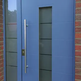Blaue moderne Haustür mit Glaseinsatz und Seitenteil an roter Ziegelwand